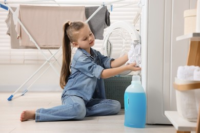 Little girl putting dirty clothes into washing machine in bathroom