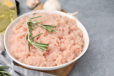 Photo of Fresh raw minced meat and rosemary in bowl on light grey textured table, closeup