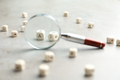 Photo of View on cubes with letters A and Q through magnifying glass at light grey stone background, closeup. Find keywords concept