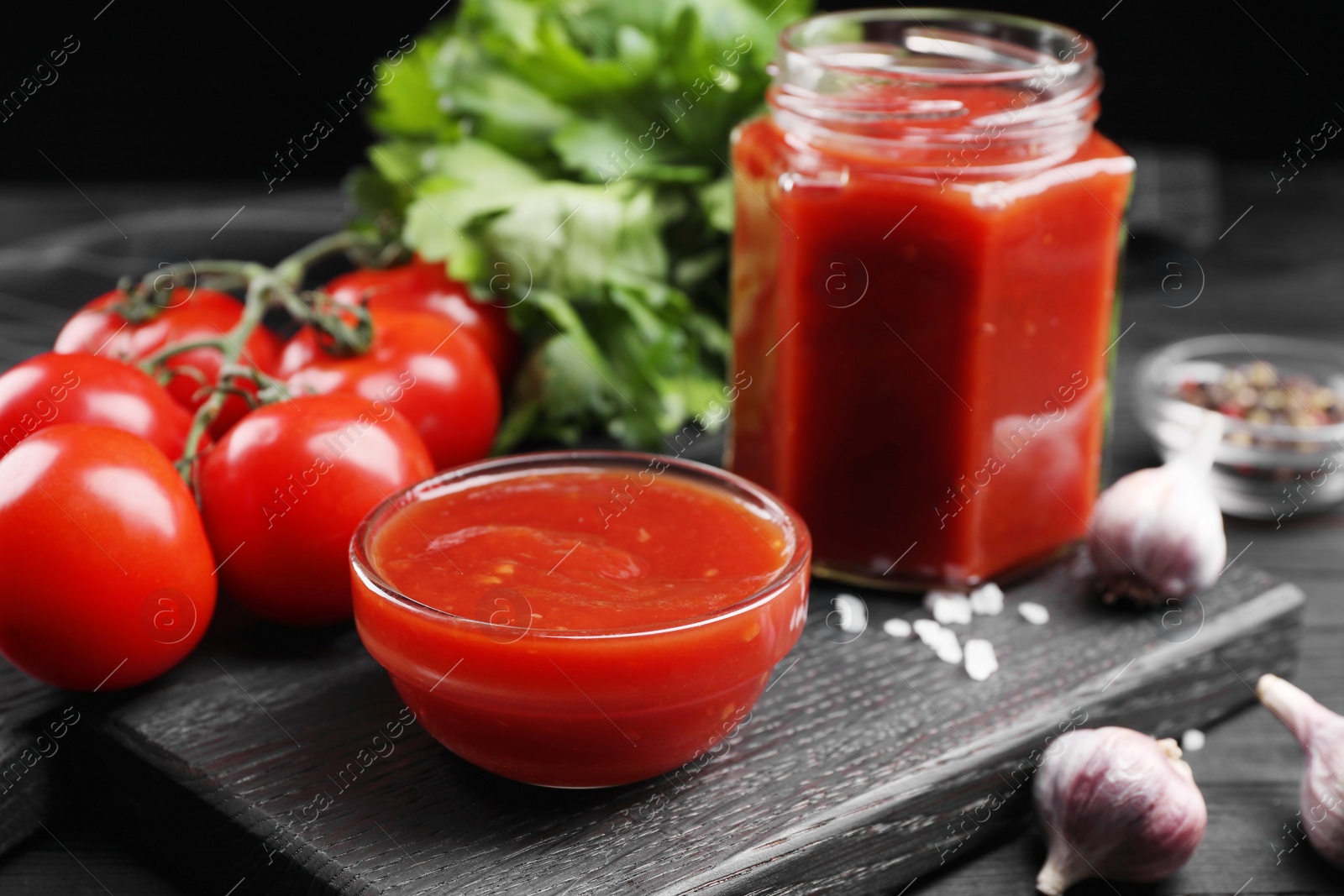 Photo of Delicious ketchup and products on black wooden table, closeup. Tomato sauce