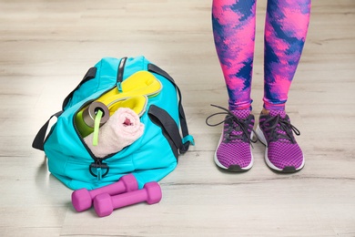 Photo of Young woman in sportswear and bag with gym equipment indoors