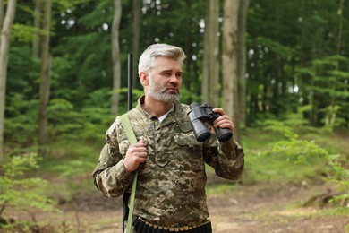 Photo of Man with hunting rifle and binoculars wearing camouflage in forest