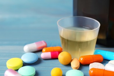 Measuring cup with syrup and pills on light blue wooden table, space for text. Cold medicine