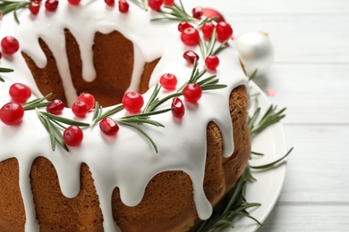 Photo of Traditional Christmas cake decorated with glaze, pomegranate seeds, cranberries and rosemary on white table, closeup
