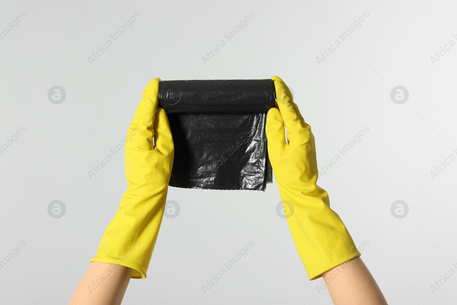 Photo of Janitor in rubber gloves holding roll of black garbage bags on light grey background, closeup