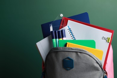 Photo of Backpack with different school stationery near chalkboard, closeup