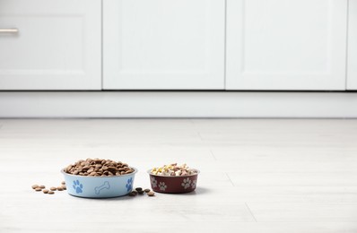 Photo of Bowls with dry dog food on white floor indoors, space for text