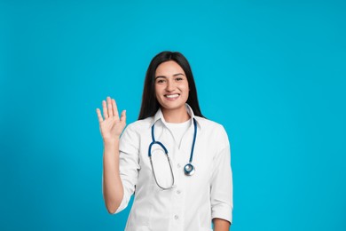 Photo of Happy female doctor waving to say hello on light blue background
