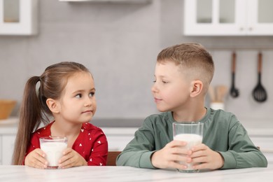 Photo of Cute children with glasses of milk at white table in kitchen