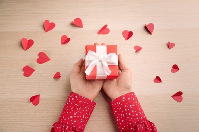 Photo of Woman holding beautiful gift box at wooden table, top view. Valentine's Day celebration