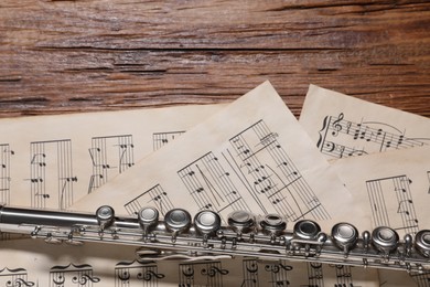 Photo of Sheets with musical notes and flute on wooden table, flat lay