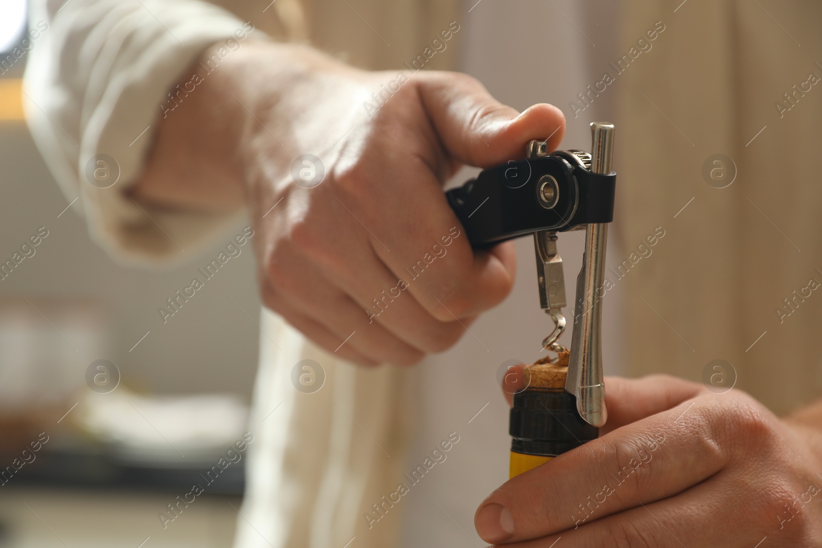 Photo of Man opening wine bottle with corkscrew on blurred background, closeup