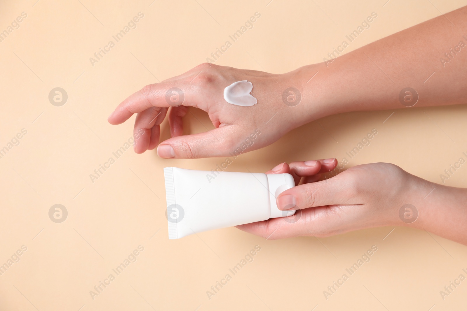 Photo of Woman with tube of hand cream on beige background, top view