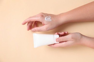 Woman with tube of hand cream on beige background, top view