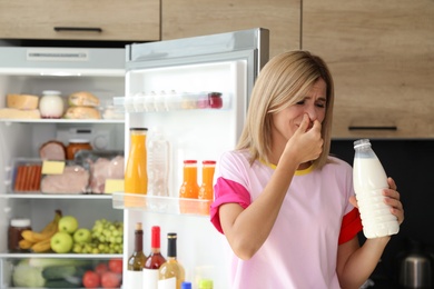 Woman taking bottle with old milk out of refrigerator in kitchen