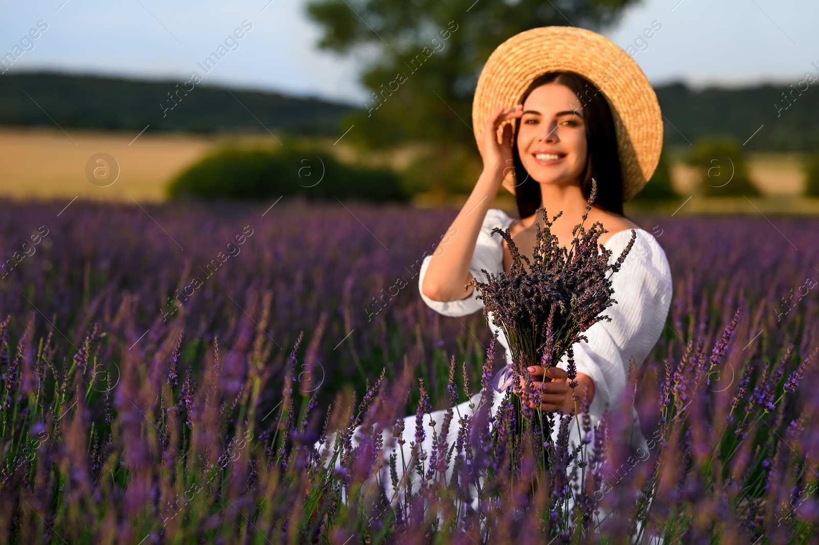 Photo of Beautiful young woman with bouquet sitting in lavender field