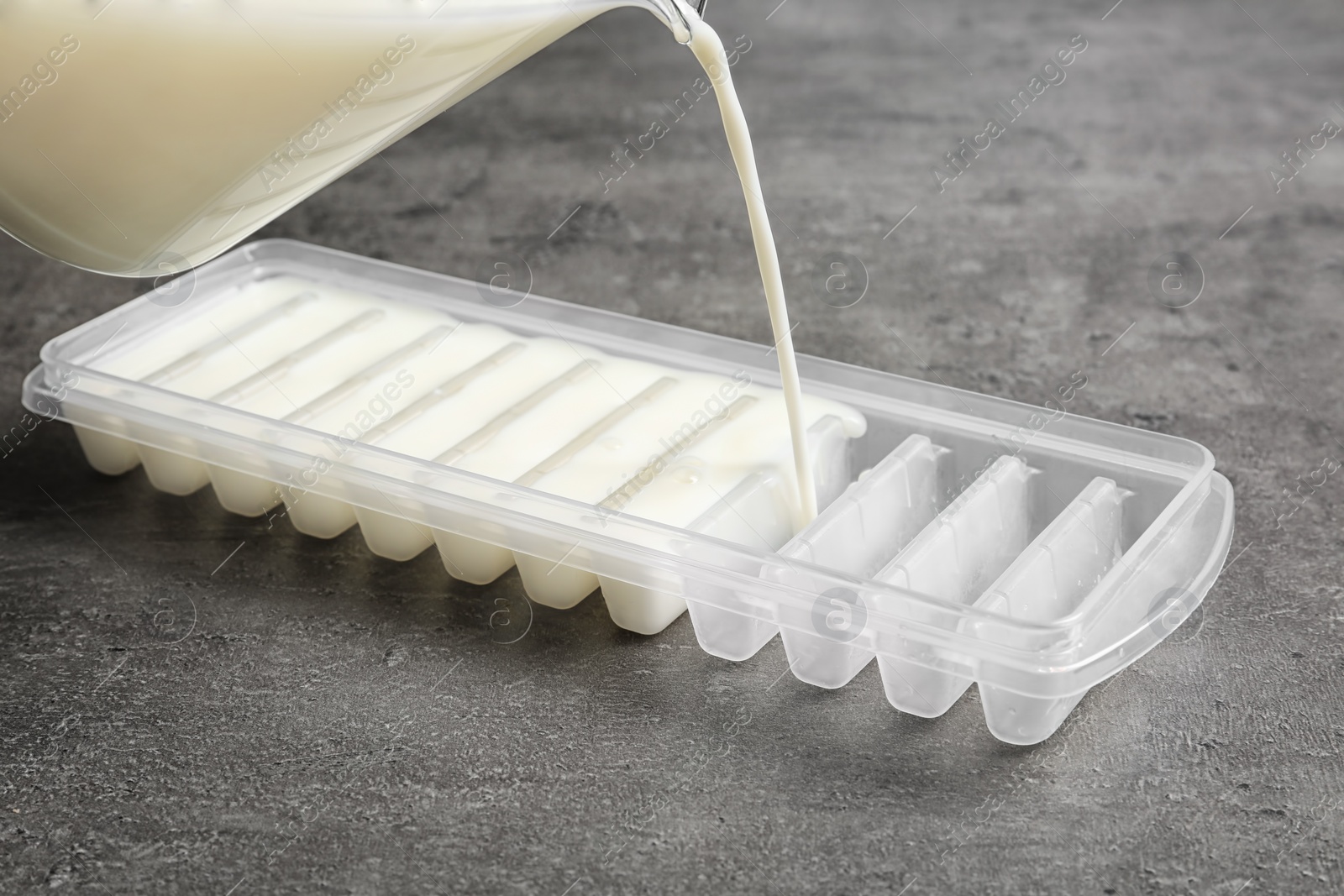 Photo of Pouring milk into ice cube tray on grey table