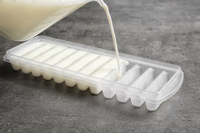 Pouring milk into ice cube tray on grey table