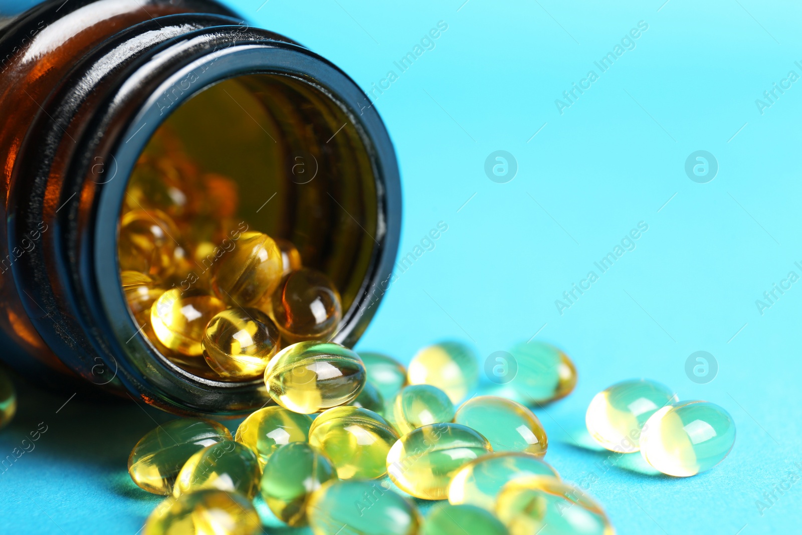 Photo of Medical bottle and yellow capsules on light blue background, closeup. Space for text