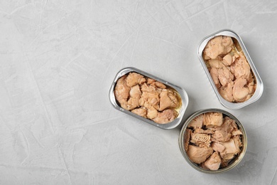 Photo of Open tin cans with tuna and cod liver on grey table, flat lay. Space for text