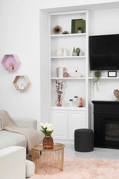 Photo of Stylish room interior with beautiful fireplace, TV set, sofa and shelves with decor