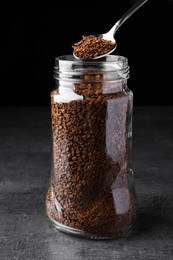 Photo of Instant coffee and spoon above glass jar on grey table against black background