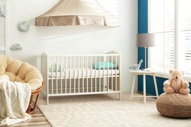 Photo of Cute nursery interior with comfortable crib near white wall