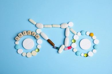 Photo of Word Doping and bicycle made of pills on light blue background, flat lay