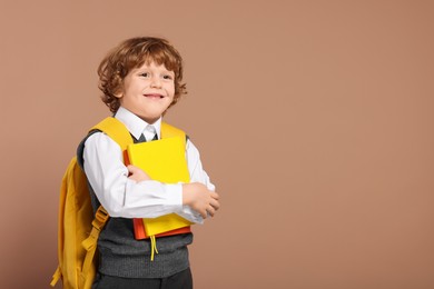 Photo of Happy schoolboy with backpack and books on brown background, space for text