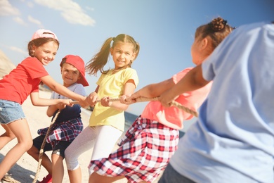 Photo of Cute children pulling rope during tug of war game on beach. Summer camp