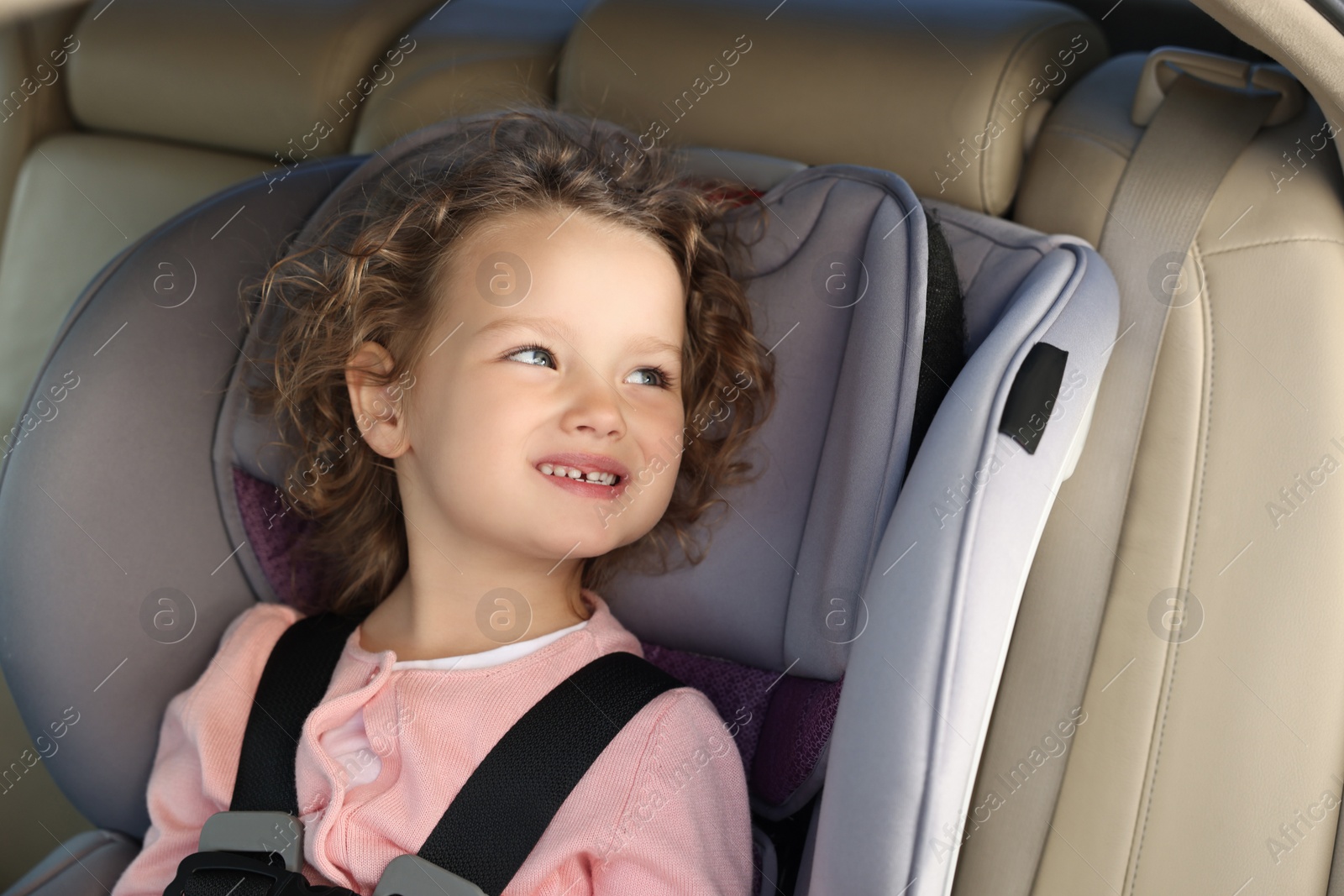 Photo of Cute little girl sitting in child safety seat inside car