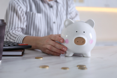 Photo of Woman with piggy bank at marble table indoors, closeup