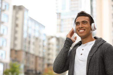 Photo of Portrait of handsome young African-American man with headphones listening to music on city street. Space for text