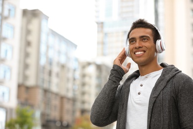 Portrait of handsome young African-American man with headphones listening to music on city street. Space for text