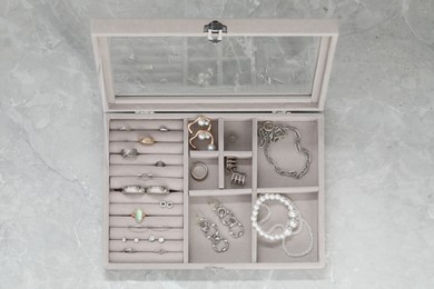Photo of Jewelry box with many different accessories on light grey table, top view