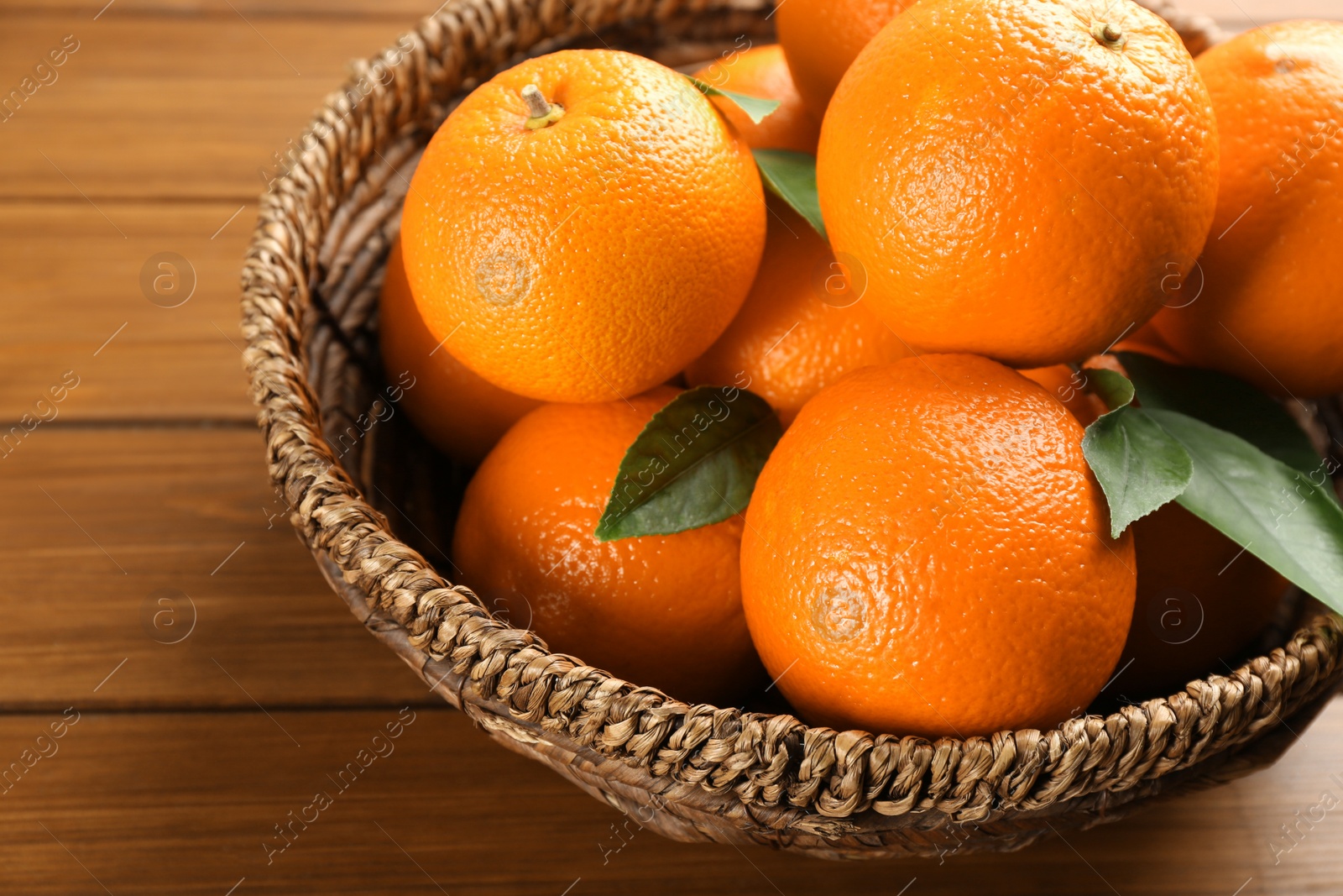 Photo of Delicious ripe oranges in wicker bowl on wooden table, closeup