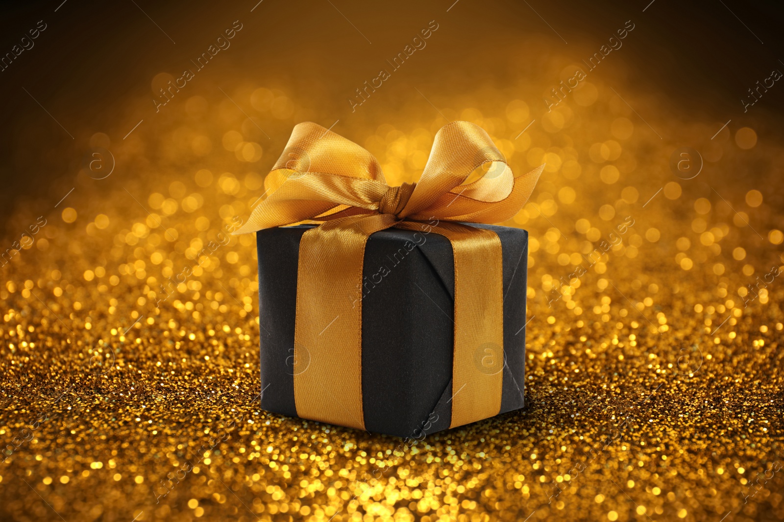 Image of Beautiful gift box on shiny golden glitters. Bokeh effect 