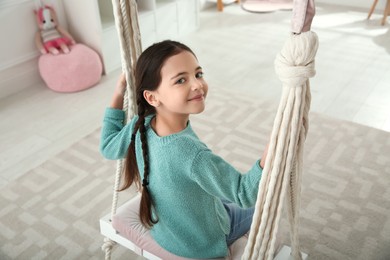 Photo of Cute little girl playing on swing at home