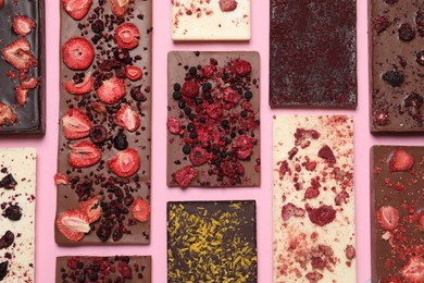 Photo of Different chocolate bars with freeze dried fruits on pink background, flat lay