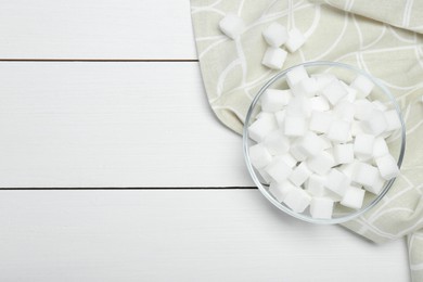 Photo of Many sugar cubes in glass bowl on white wooden table, top view. Space for text