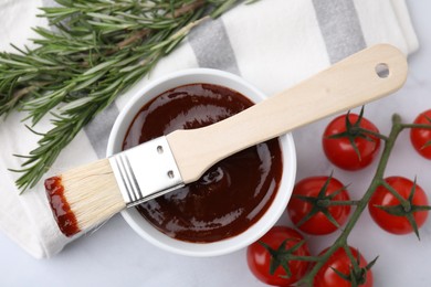 Marinade in bowl, basting brush, tomatoes and rosemary on white table, flat lay