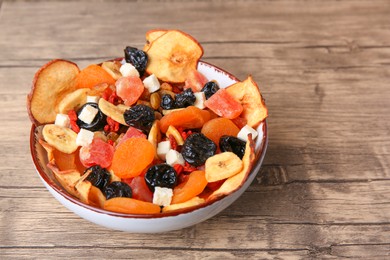 Bowl with different tasty dried fruits on wooden table. Space for text