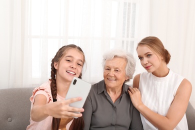 Photo of Happy sisters taking selfie with their grandmother at home