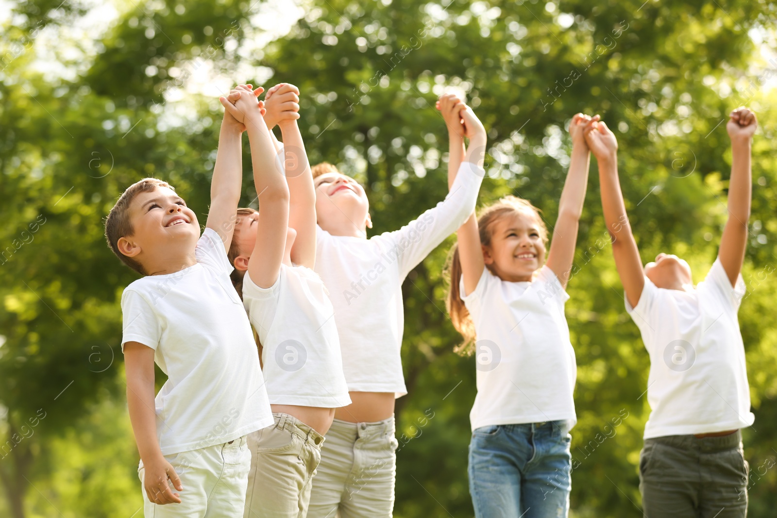 Photo of Group of children holding hands up in park. Volunteer project