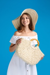 Beautiful young woman with stylish straw bag on light blue background