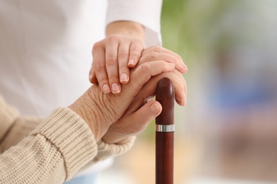 Photo of Nurse comforting elderly woman with cane against blurred background, closeup. Assisting senior generation