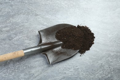Photo of Metal shovel with fertile soil on gray textured surface, above view