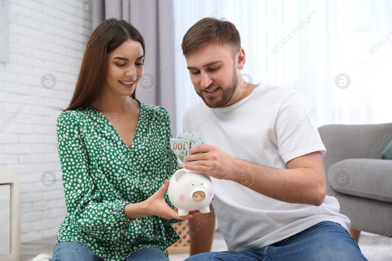 Photo of Beautiful young couple with piggy bank and money at home