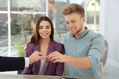 Real estate agent giving new house key to couple at table in office