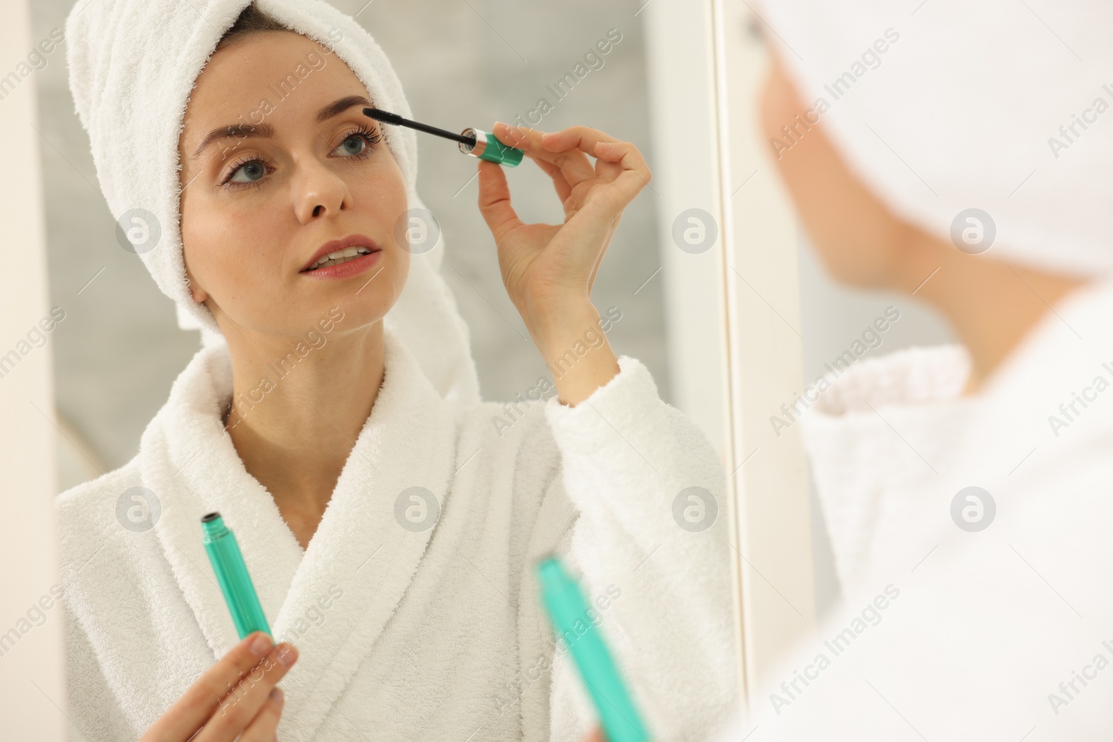 Photo of Beautiful woman applying mascara near mirror in bathroom